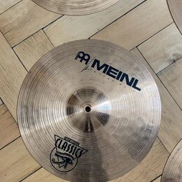Fotografie zobrazuje dva kovové činely v tradičním zlatavě hnědém odstínu s viditelným rýhováním. Na spodním činele je nápis MEINL a logo značky, dál…