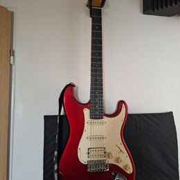 Červená elektrická kytara typu Stratocaster s bílým pickguardem a hnědým hmatníkem. Na hlavě je vidět nápis Squier. Kytara má tři snímače, pětistupňo…