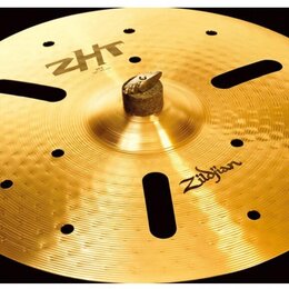 Zlatý kovový činel s výrazným kladivečkováním a třemi oválnými otvory. Na povrchu jsou nápisy ZHT a Zildjian. Činel je umístěn na černém držáku.