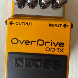Žlutý efekt pedál s kovovým horním panelem a čtyřmi chromovanými oválnými knoflíky. Na přední straně jsou nápisy OUTPUT, INPUT a velký text OverDrive…