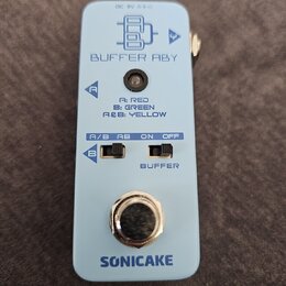Světle modrý efekt pedál s nápisy BUFFER ABY a SONICAKE. Na horní části je schéma zapojení, v prostřední části přepínače A/B AB a ON OFF s dopisem A:…