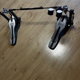 Dvojpedál na bicí v černé a stříbrné barvě s kovovými komponenty. Na obou šlapkách je umístěno logo MAPEX. Povrch pedálů vykazuje známky běžného použ…