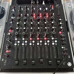 Černý DJ mixér s mnoha ovládacími prvky, potenciometry a posuvníky. Na panelu jsou viditelné nápisy jako MASTER, FILTER, CUT / BOOST, CUE A, CUE B a…