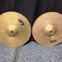 Dvě mosazné činely s viditelným opracováním povrchu. Oba mají nápis 13" Cymbal a logo flash CYMBALS. Povrch pravého činele vykazuje více drobných skv…