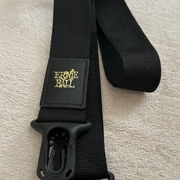 Černý textilní popruh na hudební nástroj s plastovými koncovkami. Na středním čtvercovém poli je žlutý nápis ERNIE BALL. Povrch popruhu i plastových…