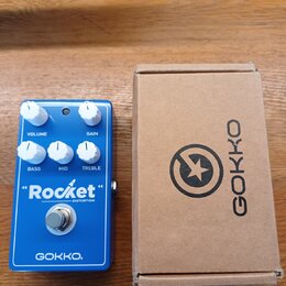 Modrý efekt pedál s nápisy "Rocket" DISTORTION a GOKKO. Na horní straně jsou čtyři bílé ovládací knoflíky s popisky VOLUME, GAIN, BASS, MID a TREBLE.…