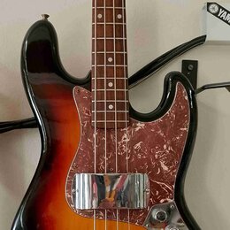 Elektrická basová kytara s korpusem v barevném přechodu od černé přes červenou k žluté. Nástroj má hnědý hmatník a pickguard s červeně-hnědým mramoro…