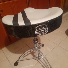 Černý bubeníkůvstolec se sedákem ve tvaru lednice. Horní plocha sedáku je bílá s dvěma černými pruhy, boční strana je černá s glitry a nápisem MAPEX™…