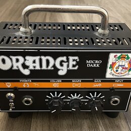 Černý kompaktní kytarový zesilovač s kovovou rukojetí nahoře. Na předním panelu je bílý nápis ORANGE a model Micro Dark. Zařízení má čtyři ovládací p…