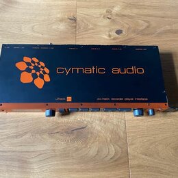 Černý rackový audio rozhraní s oranžovými detaily. Na horním panelu je oranžové logo a nápis cymatic audio, v dolní části nápisy uTrack 24 a 24-track…