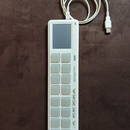 Bílá MIDI kontrolér s názvem KORG nanoPAD2. Zařízení má mřížku 16 čtvercových padů v rozložení 4x4, malý displej v horní části a řadu ovládacích tlač…