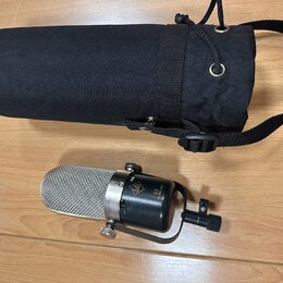 Stříbrný kondenzátorový mikrofon s černým tělem a kovovým držákem. Na těle je viditelné logo značky AKG a nápis R1 ACM-180. Vedle mikrofonu je černý…