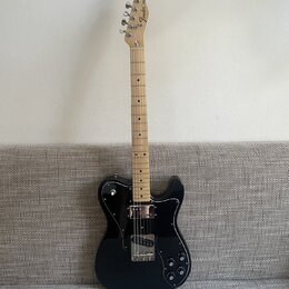 Černá elektrická kytara s černým pickguardem a světlým hnedým hmatníkem. Na hlavě je nápis Fender Mexico. Kytara má dva snímače a tři ovládací knoflí…