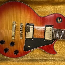 Elektrická kytara typu Les Paul v červeno-žlutém sunburst provedení s viditnou strukturou dřeva. Nástroj má dva snímače s krémovými kryty, zlatý most…