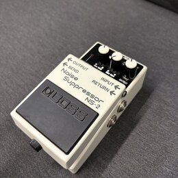 Bílý efekt pedál Boss Noise Suppressor NS-2 v kompaktním kovovém provedení s černým gumovým spínacím pedálem. Na horní části jsou čtyři bílé ovládací…