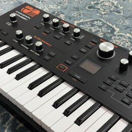 Černý klávesový syntetizátor s bílými a černými klávesami. Na horním panelu jsou nápisy ASM, SONIC MACHINES a model HYDRASYNTH EXPLORER. Přístroj obs…
