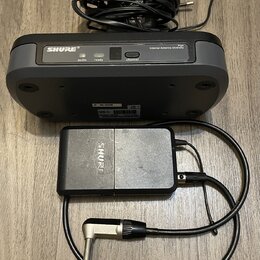 Černý bezdrátový vysílač a přijímač značky SHURE. Na horním zařízení je nápis SHURE, model PG4 a popis Internal Antenna Diversity s kontrolkami audio…