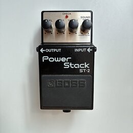 Kytarový efekt pedál značky BOSS, model Power Stack ST-2. Zařízení má černý kovový korpus s nápisy OUTPUT a INPUT u konektorů. Horní část tvoří stříb…