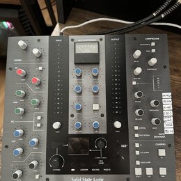 Černý rackový procesor s nápisem Solid State Logic. Zařízení obsahuje analogové VU metr, několik bílých a modrých otočných knoflíků, posuvníky a bílé…