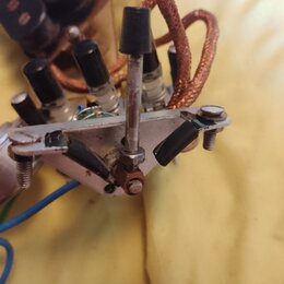Detailní pohled na vnitřní elektroniku s několika černými kondenzátory a měděným opleteným kabelem. V popředí je kovový držák s šrouby a dvěma černým…