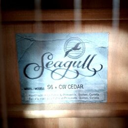 Fotografie znázorňuje štítek uvnitř akustické kytary. Na modrobílém pozadí je černé logo Seagull s vyobrazením ptáka v kruhu. Pod ním je uveden text…