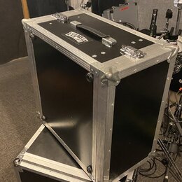 Černý transportní flightcase s hliníkovými hranami a kovovými rohy. Na horní straně je umístěna černá rukojeť a dva kovové zámky, vedle nich je nálep…