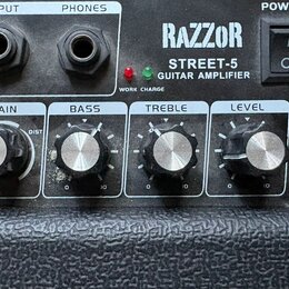 Detailní pohled na ovládací panel kytarového komba s černým texturovaným povrchem. Na panelu je nápis RAZZOR STREET-5 GUITAR AMPLIFIER, vypínač POWER…