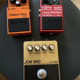 Tři kytarové efekty umístěné na černém podkladu. Vlevo je oranžový pedál s nápisy Distortion DS-1 a BOSS, vpravo červený pedál s nápisy Loop Station…