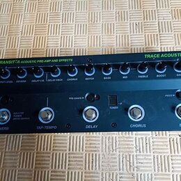 Černý předzesilovač s efekty Trace Acoustic Transit-A Acoustic Pre-Amp and Effects. Horní řada obsahuje deset otočných potenciometrů s popisky Output…