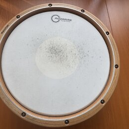 Kruhové bubení s dřevěným rámem a bílou membránou. Na membráně je nápis AQUARIAN TEXTURE COATED a v horní části dřevěného rámu je vyryto HALLVAD. Stř…