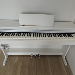 Bílé digitální piano s bílým stojanem a notovým pultem. Na horní liště nad klávesami je umístěno logo YAMAHA. Nástroj má tři st SILVER pedály a někol…