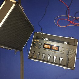 Na fotografii je kytarový procesor Boss GT-100 v bílém hliníkovém kufru s černým polstrováním. Zařízení má digitální displeje, několik ovládacích tla…