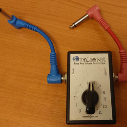 Bílý obdélníkový box s nápisem Omnisonic Tube Amp Volume Control Box a e-mailem noiseradio@man.com. Zařízení má jeden černý otočný ovladač s číslicem…