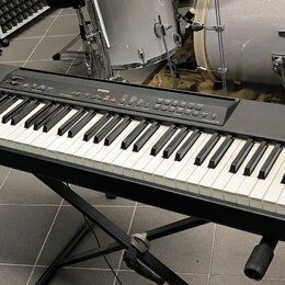 Černý digitální klavír umístěný na černém X-stojanu. Na horním ovládacím panelu je vidět bílý nápis YAMAHA a modelové označení PSR-S970. Nástroj má s…