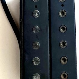 Černý humbucker s dvěma řadami šesti magnetických pólů. Povrch je viditelně opotřebovaný s četnými škrábanci a odřeninami, zejména na levé straně. Z…
