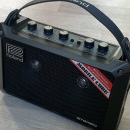 Černý přenosný stereo zesilovač s rukojetí. Na přední mřížce je bílé logo Roland a červenobílý nápis MOBILE CUBE Battery Powered Multi purpose stereo…
