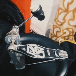 Detailní pohled na kovový pedál basového bubnu s černým plastovým stupňem. Na boku mechanismu je nápis POWERGLIDE a na stupni je bílý grafický symbol…