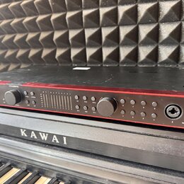 Černý elektronický přístroj s červeným lemováním předního panelu. Na levé straně je nápis "Scarlett 18i20" a několik ovládacích knoflíků. Panel obsah…