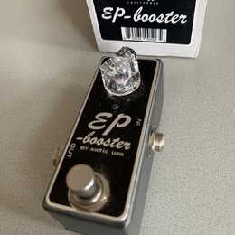 Kytarový efekt pedál v stříbrném kovovém šasi s černým horním panelem. Na panelu je bílý nápis EP-booster BY xotic usa a v pravém horním rohu označen…