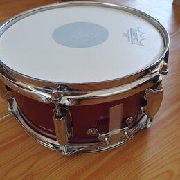 Červený snare drum s chromovaným obručováním a mechanismem. Na bílém koženu je vidět logo REMO s nápisem COATED AMBASSADOR. Nástroj vykazuje známky p…