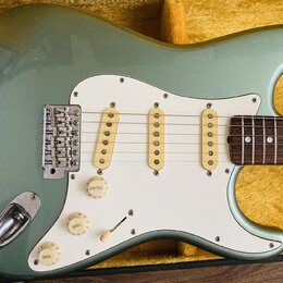 Světle zelená elektrická kytara typu Stratocaster s bílým pickguardem a třemi jednoduchými snímači. Nástroj je umístěn v otevřeném kufru s žlutým pol…