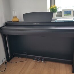 Černý digitální piano s nápisem YAMAHA na přední straně. Nástroj má uzavřenou klaviaturu, tři pedály a na horní desce je umístěn notový stojan. Povrc…