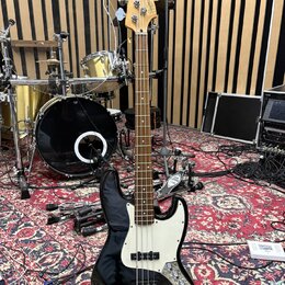 Černá elektrická basová kytara s bílým pickguardem a světle hnědým hmatníkem. Na hlavě je nápis Fender Jazz Bass. Tělo je v lesklém černém provedení,…