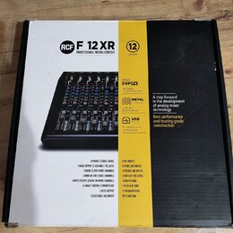 Fotografie znázorňuje krabici od míchací konzole s nápisem RCF F 12 XR PROFESSIONAL MIXING CONSOLE. Na obalu je vyobrazen černý mixážní pult a texty…