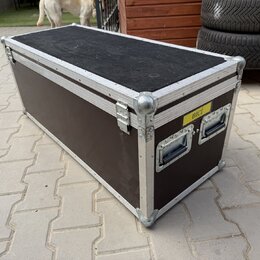Černý transportní flightcase s hliníkovými hranami a kovovými rohy. Na čelní straně jsou dvě madla a žlutý štítek s nápisem BICÍ. Povrch vykazuje běž…