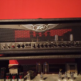 Černý kytarový kombozesilovač s kovovou mřížkou a logem Peavey v horní části. Na ovládacím panelu jsou nápisy ValveKing TUBE AMPLIFIER a VK 100. Pane…