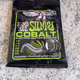Zavřené balení kytarových strun v černé fólii. Na obalu je nápis ERNIE BALL SLINKY COBALT ELECTRIC GUITAR STRINGS a seznam průměrů 10, 13, 17, 26, 36…
