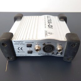Stříbrná DI box s černými gumovými nárožníky. Na zadním panelu jsou nápisy BEHRINGER®, ULTRA-DI, MODEL DI100, ATTENUATION, INPUT a LINK, dále značka…