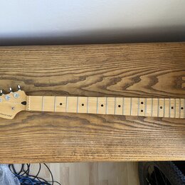 Světle hnědý javorový krk elektrické kytary s hmatníkem ze stejného materiálu. Na hlavě je černé logo Fender a nápis STRATOCASTER. Nástroj má stříbrn…