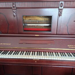 Hnědé dřevěné piano s klaviaturou a dekorativními výřezy na horním panelu. Na levé straně nad klávesami je nápis HUPFELD'S PHONOLISZT a na pravé stra…